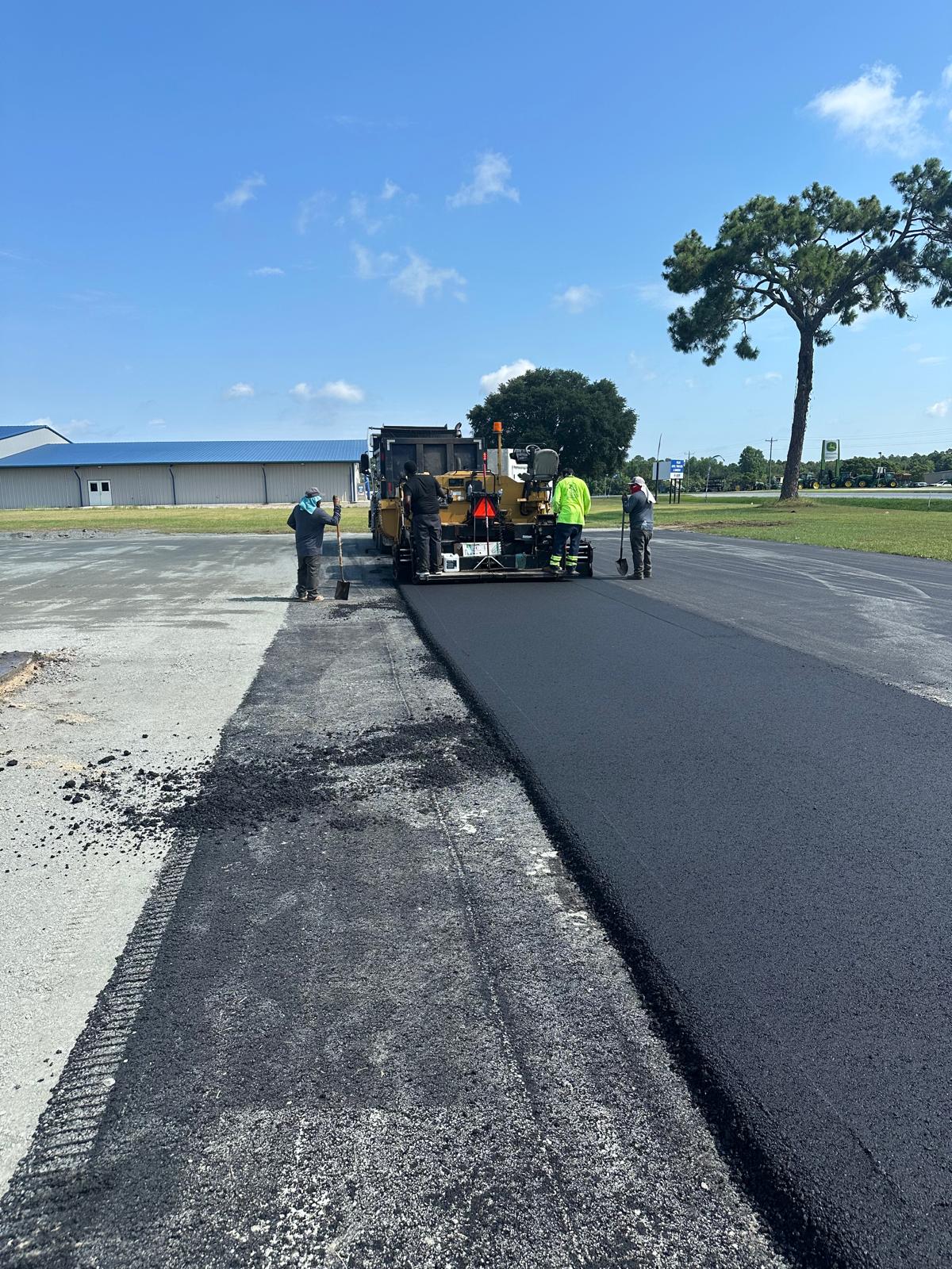 Paving crew placing a new asphalt lane beside an industrial building